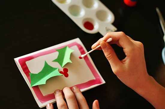 Painting holly berries on a Christmas card @makeandtakes.com