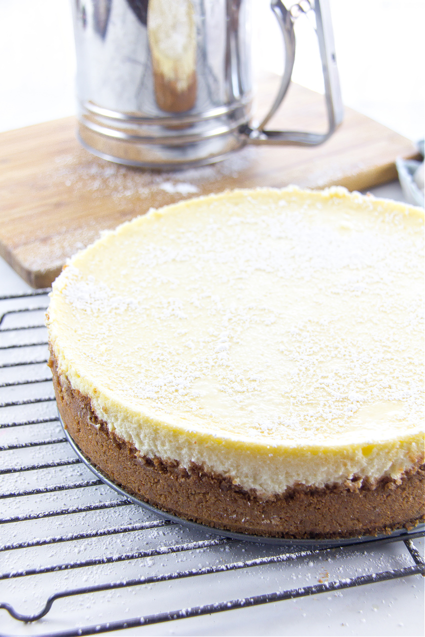 a cheesecake on a wire rack with confectioners sugar on top