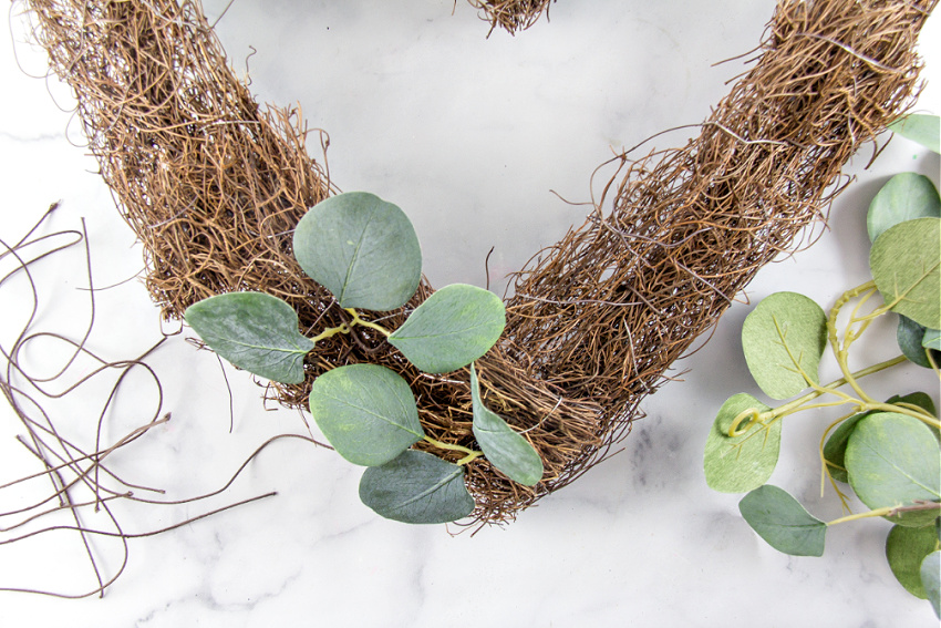 adding green stems to a natural wreath