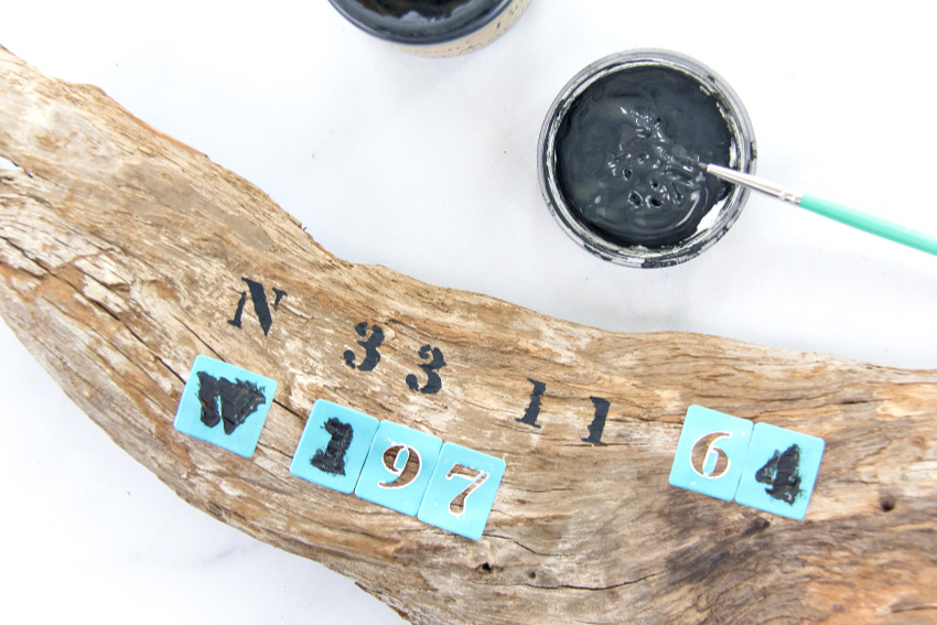 painting black numbers on a piece of driftwood