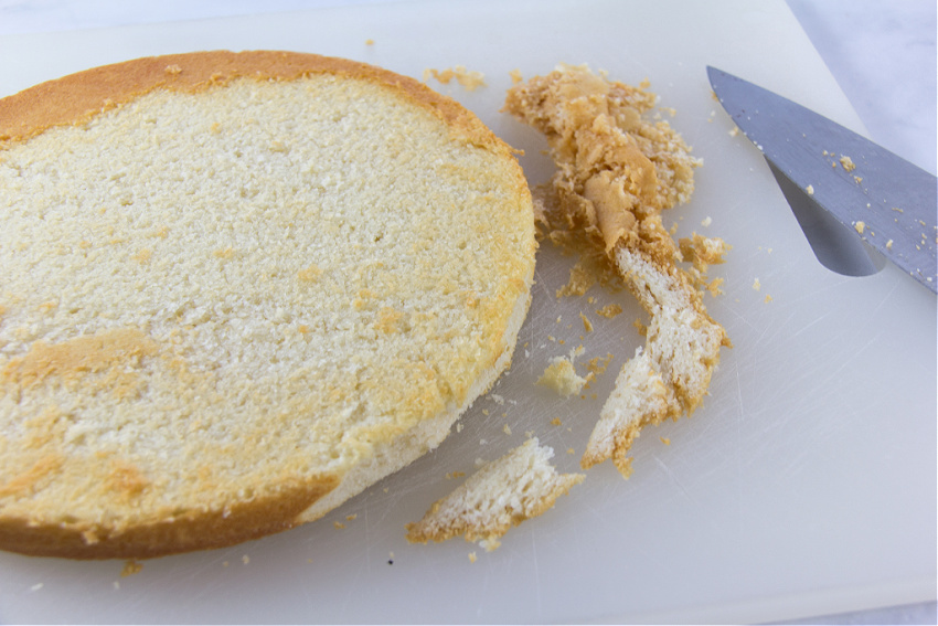 a white cake on a cutting board with the cooked edges being trimmed away