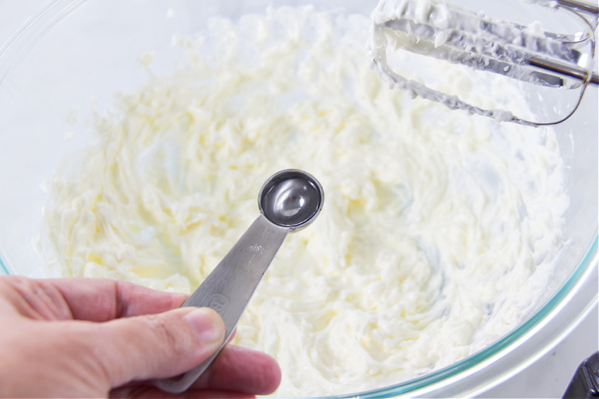 clear coconut extract in a silver teaspoon being added to a cake mix batter