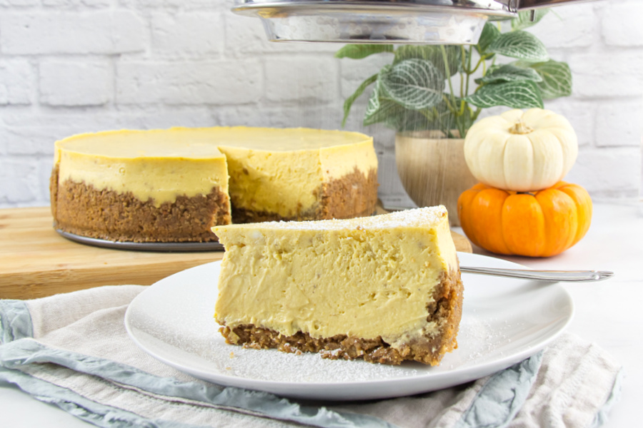 a slice of gluten free pumpkin cheese on a plate with the cheesecake on a board behind it