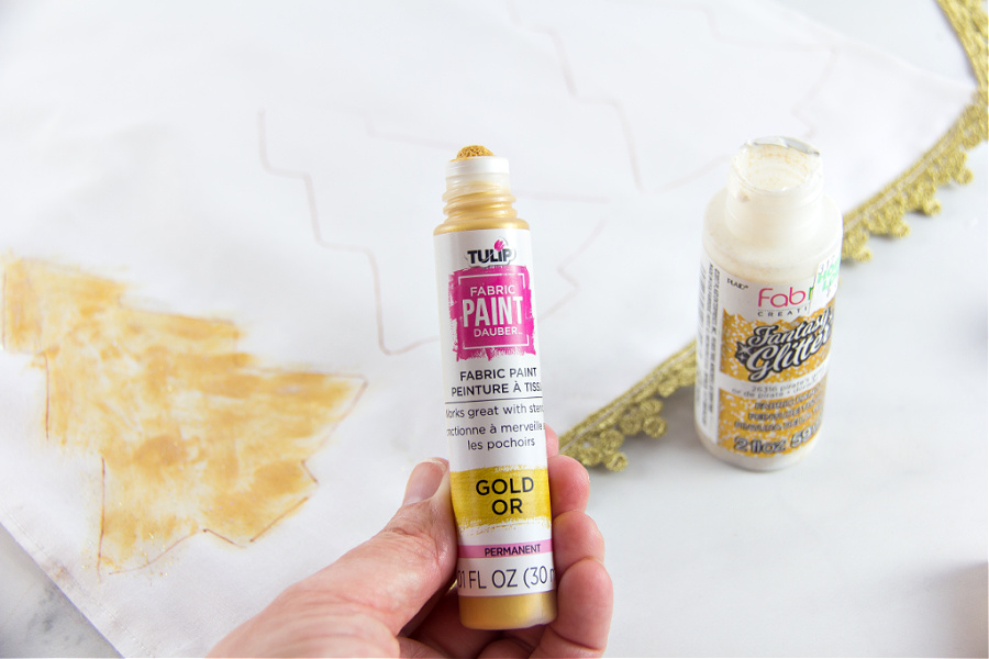 gold paint being used to paint gold christmas trees on a table runner