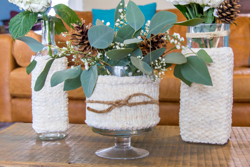assorted vases wrapped in knit cozies and filled with winter flower arrangements