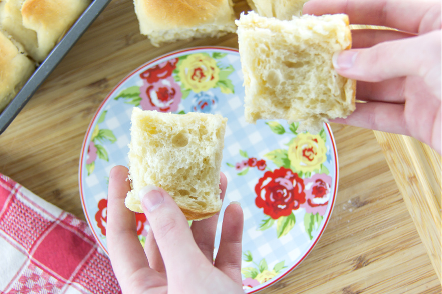 hands holding a homemade dinner roll broken in half