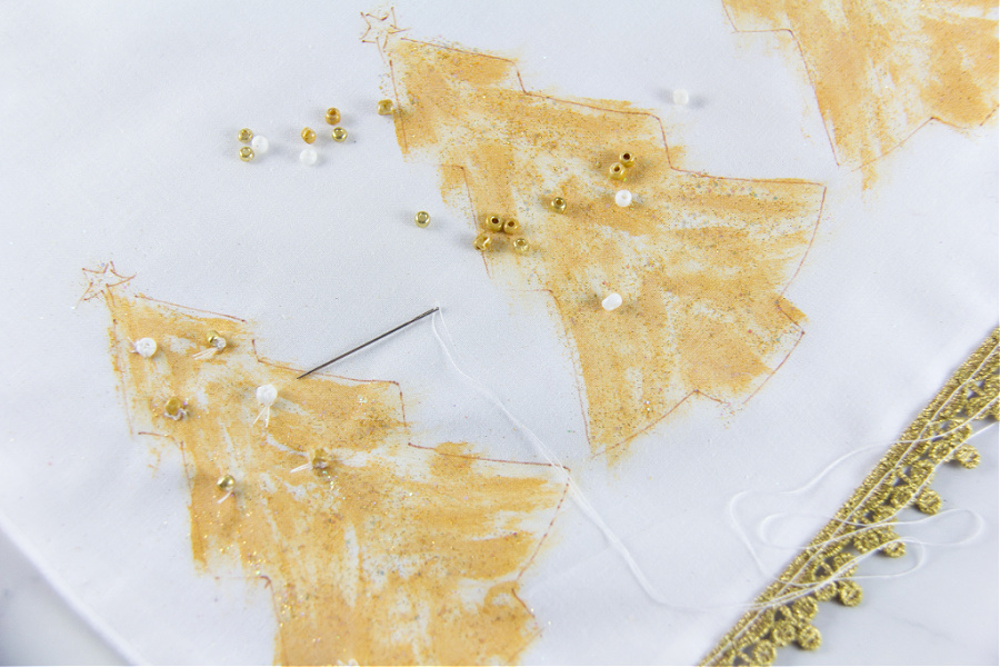 beads being sewn onto gold christmas trees on a table runner