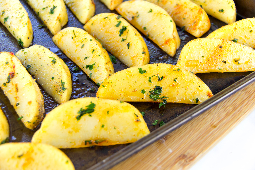 potato wedges on a baking tray with oil, seasoning, and parsley