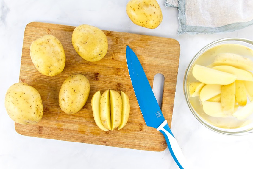 yukon gold potatoes being cut into wedges on a cutting board