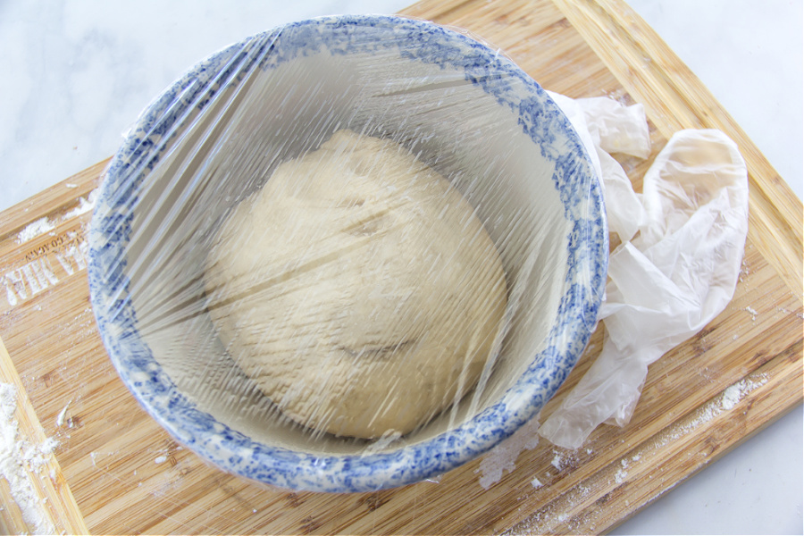 bread dough rising in a bowl covered with plastic wrap