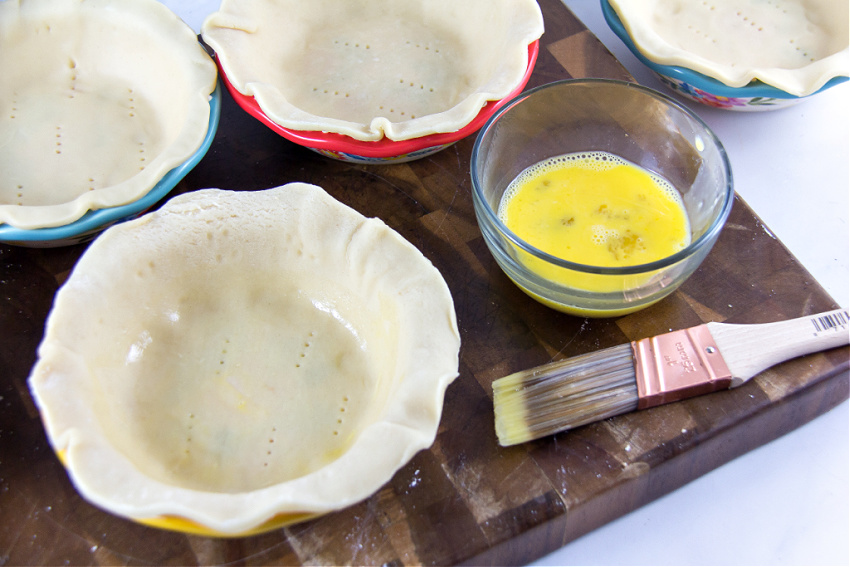 egg being brushed over pie crusts to prevent them from getting soggy