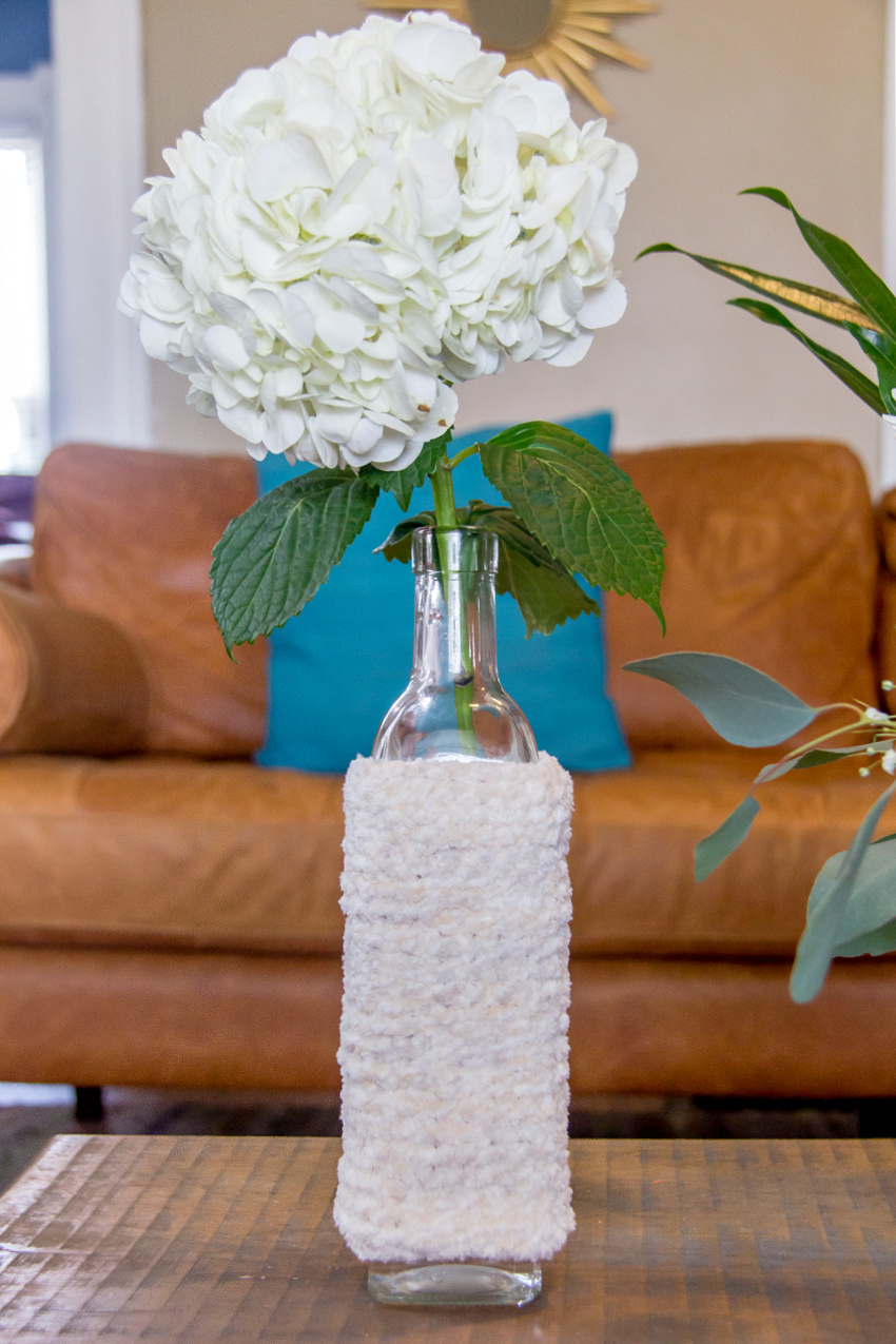 a glass bottle wrapped in a knit cozy with a singular flower