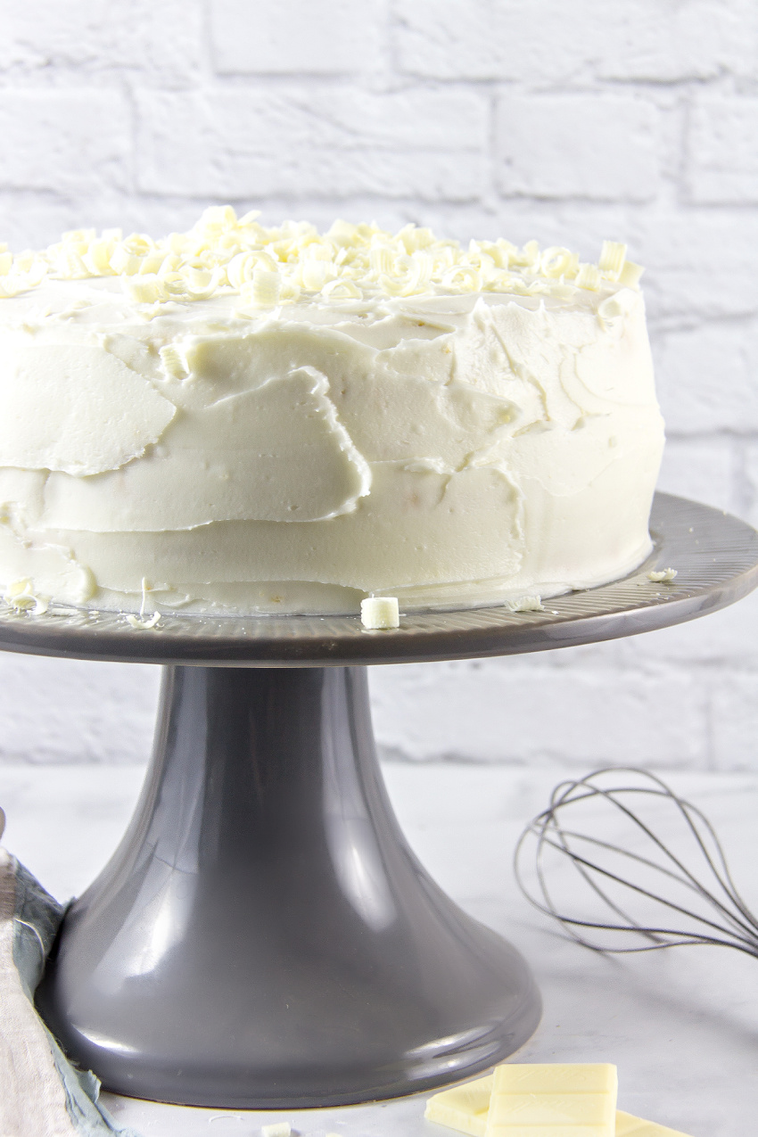 a white cake on a grey cake stand with baking tools