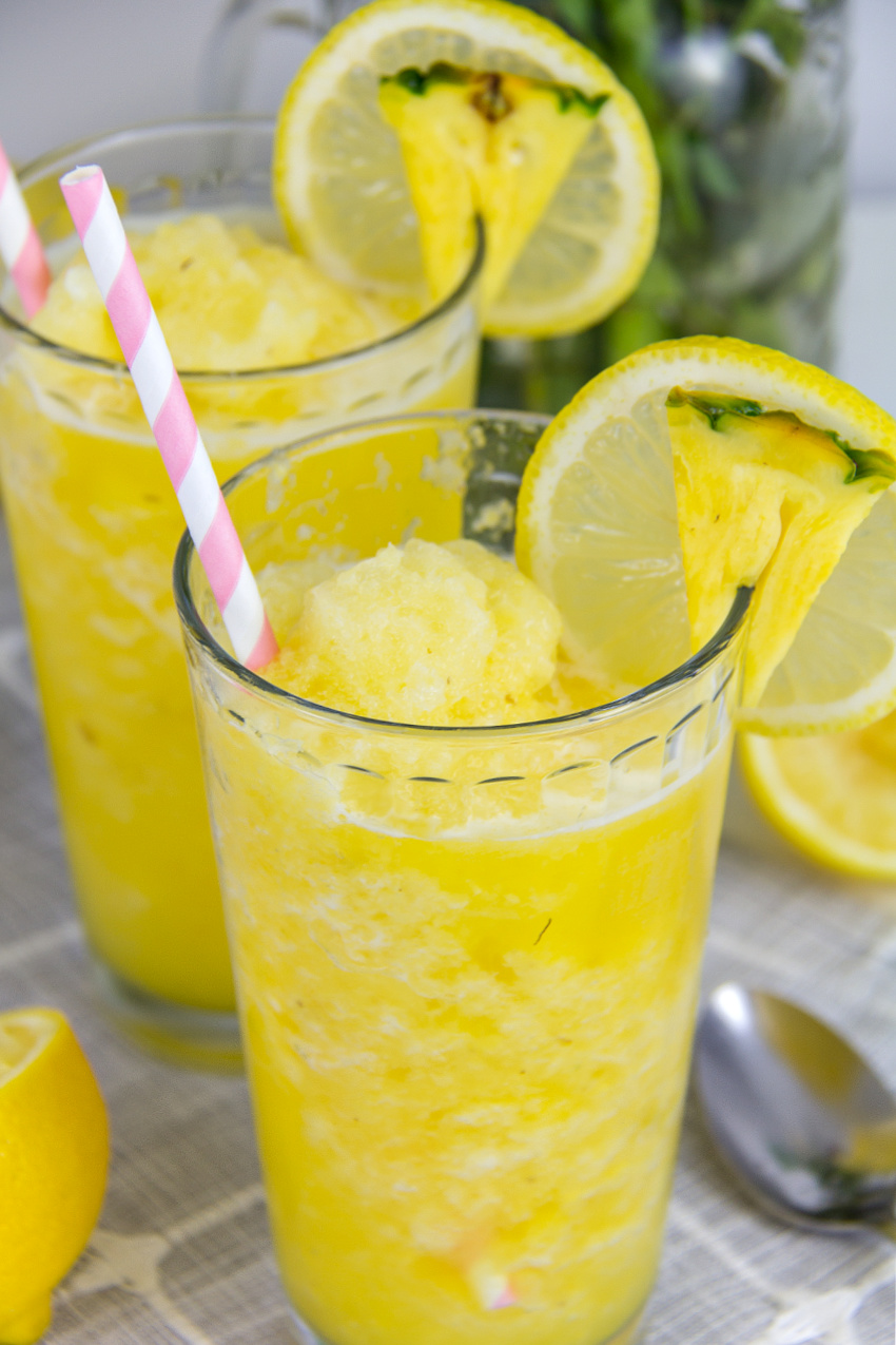 pineapple lemonade slushies in a glass with lemon and pineapple garnish and a pink straw