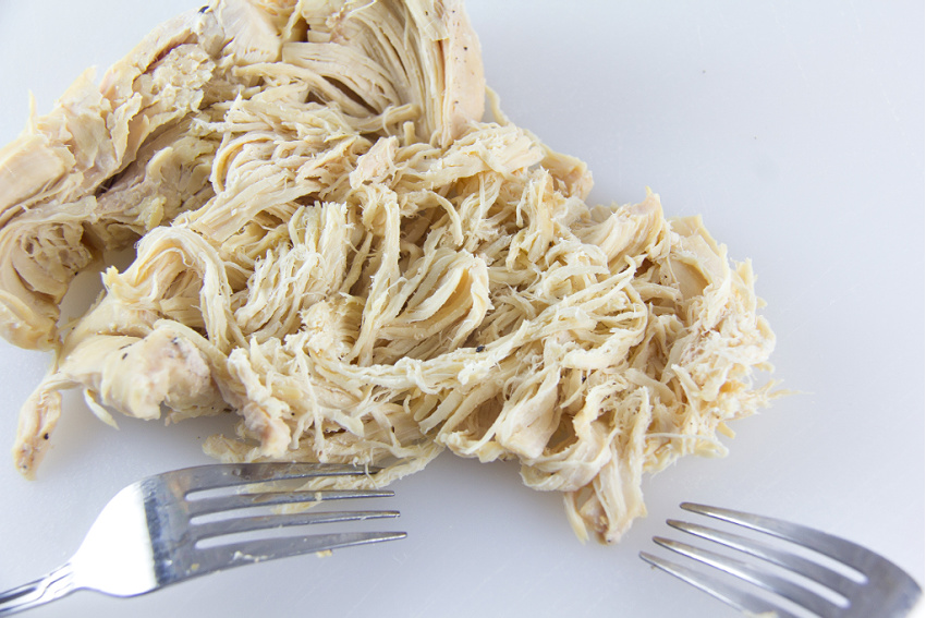 chicken being shredded on a white cutting board with two forks